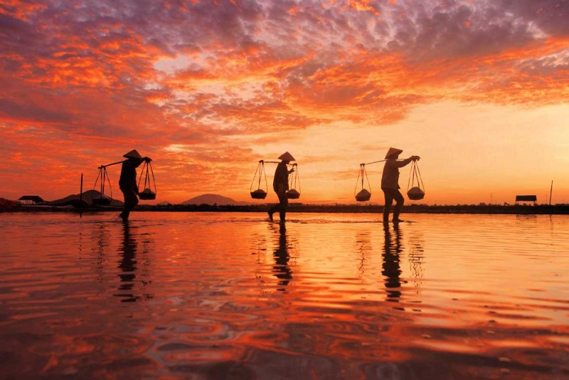 Hon Khoi Salt Fields at Dawn with Workers Silhouetted Silhouetted salt workers carrying baskets on shoulder at dawn over Hon Khoi Salt Fields