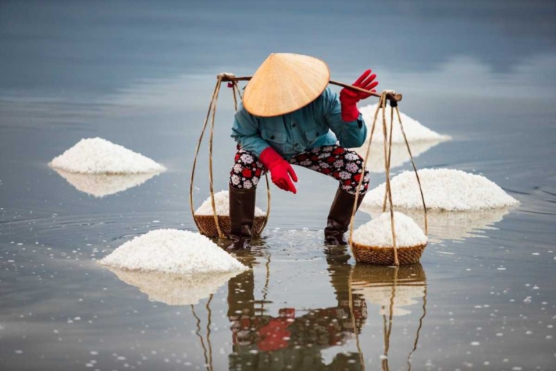 Salt Worker at Hon Khoi Salt Fields with Salt Piles Salt worker carrying baskets of salt near piles at Hon Khoi Salt Fields, Nha Trang