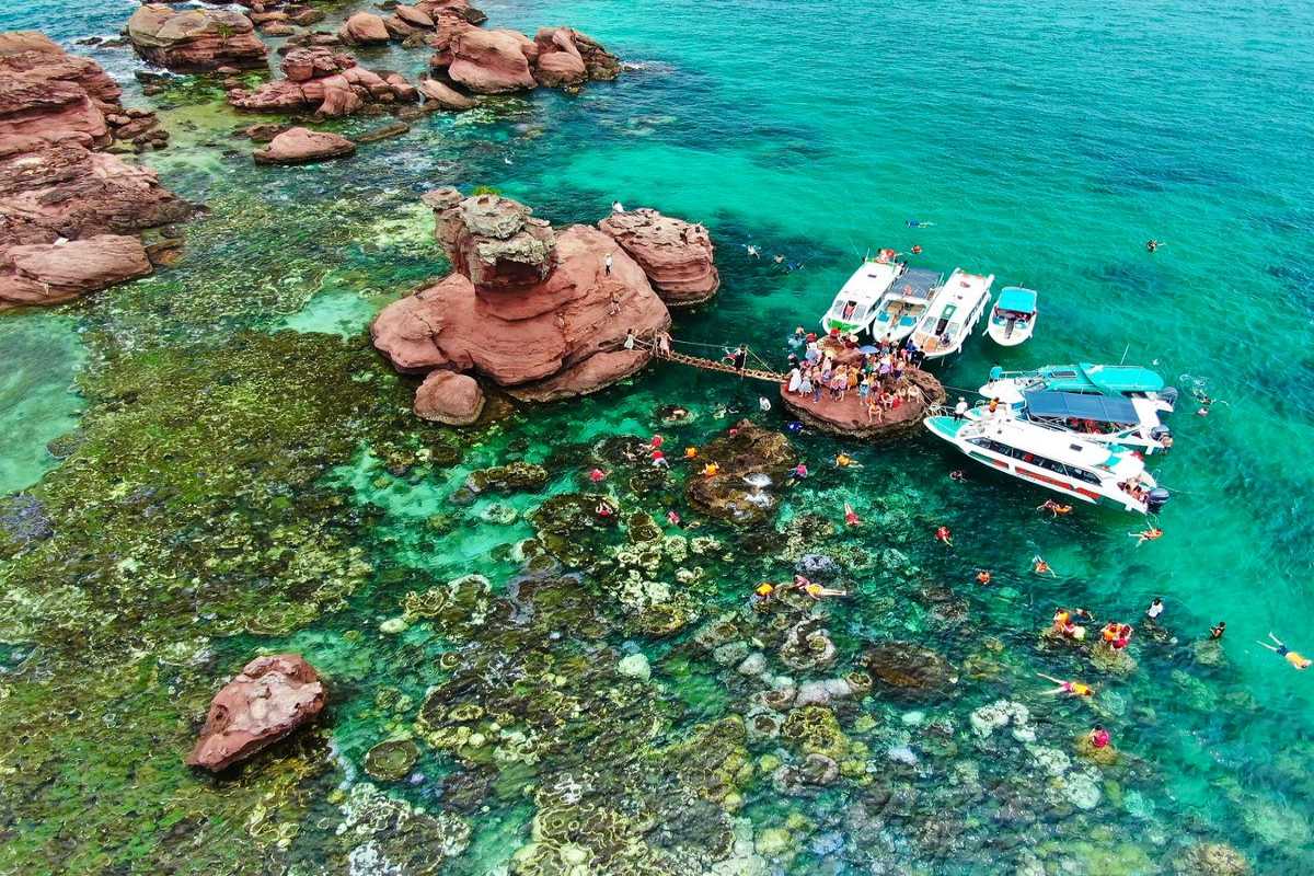 Snorkelers explore vibrant coral reefs near red rock formations at Gam Ghi Island during the Adventure Day & Night Cruise.
