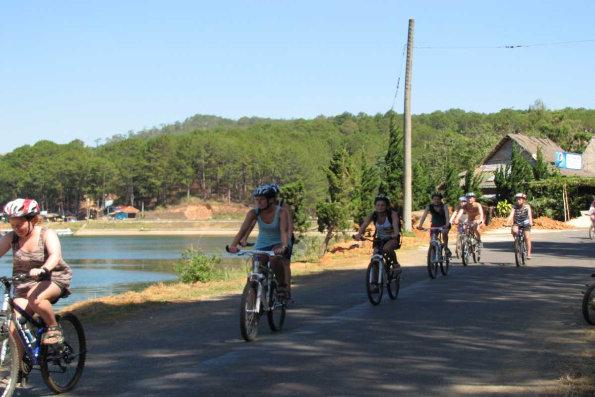 Travelers cycling along a rural path beside a lake on the Nha Trang countryside biking tour