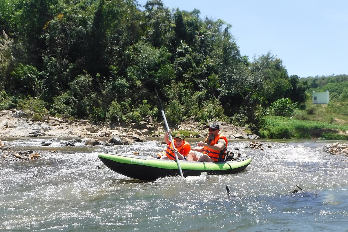 Two tourists paddling through rocky rapids during the Nha Trang full day rafting tour with scenic views.